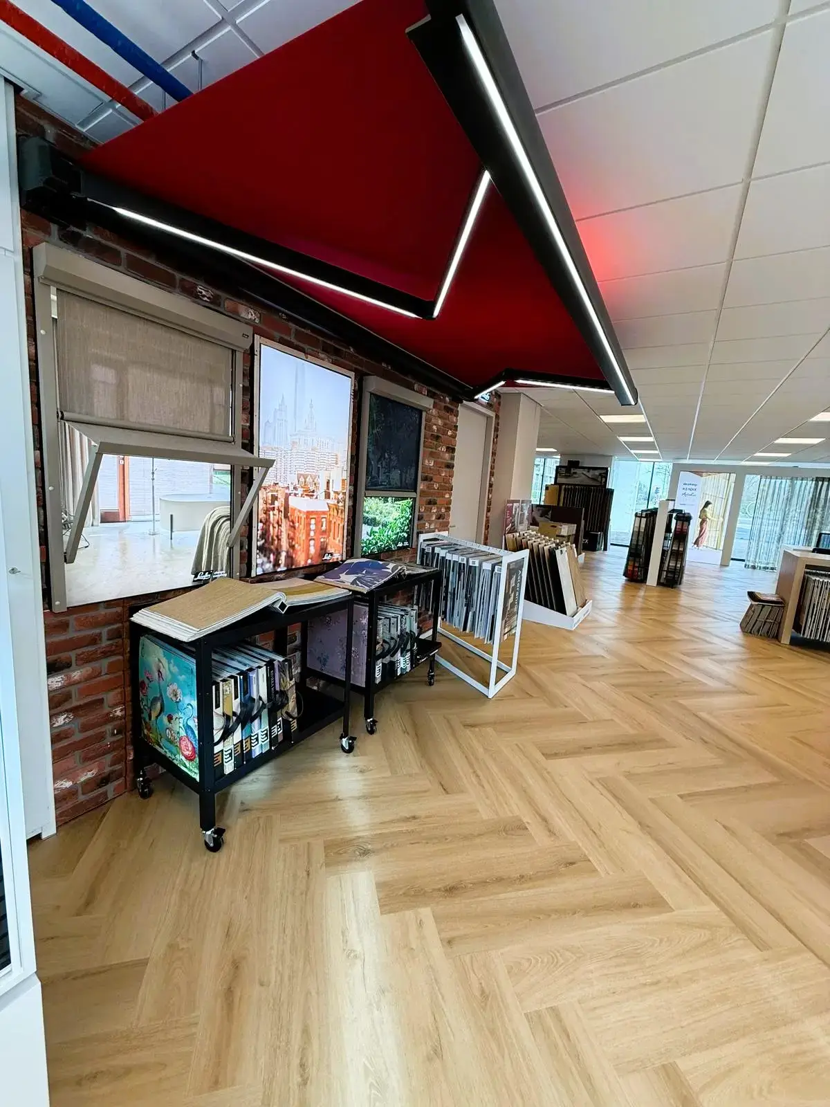 Uitgeklapt rood zonnescherm boven een stenen wand met zonwering en stalenboeken, in de showroom van Leeuwenkamp