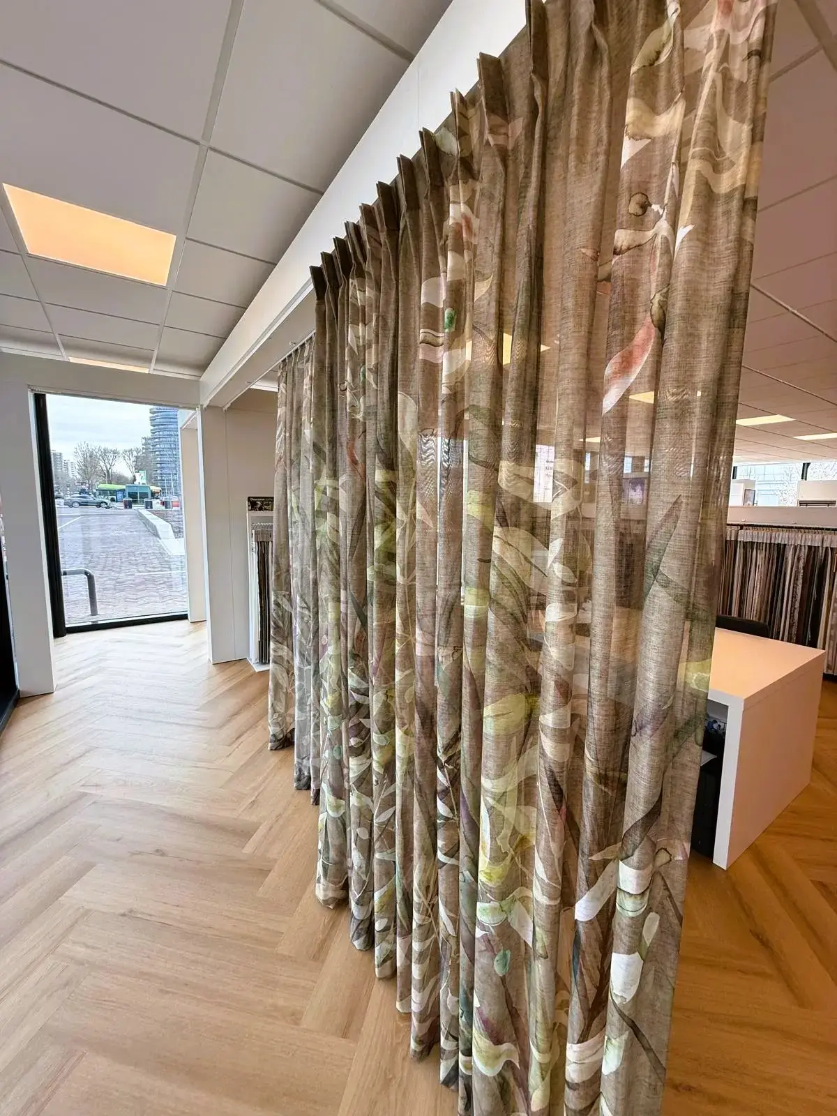 Een lang gordijn met bladerprint hangt op ware grootte in de showroom van Leeuwenkamp