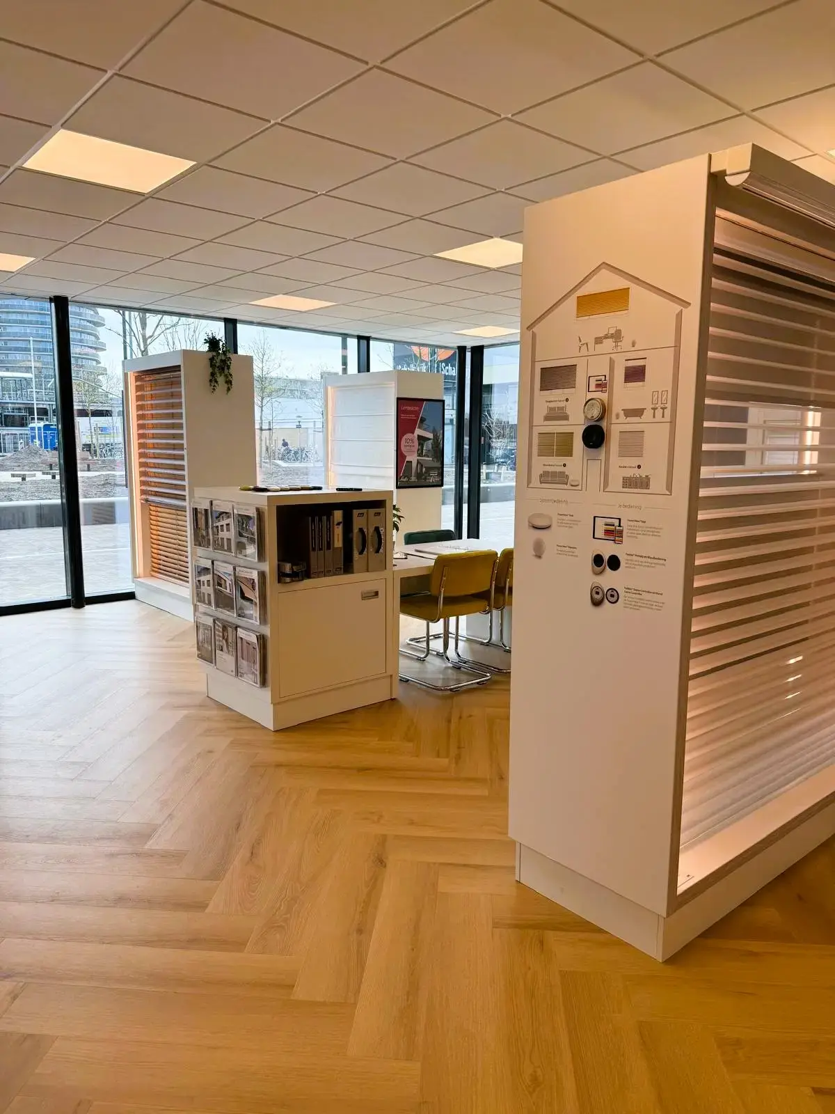 Presentatiewand met lichtdoorlatende raamdecoratie en bediening, naast een adviestafel in de showroom van Leeuwenkamp