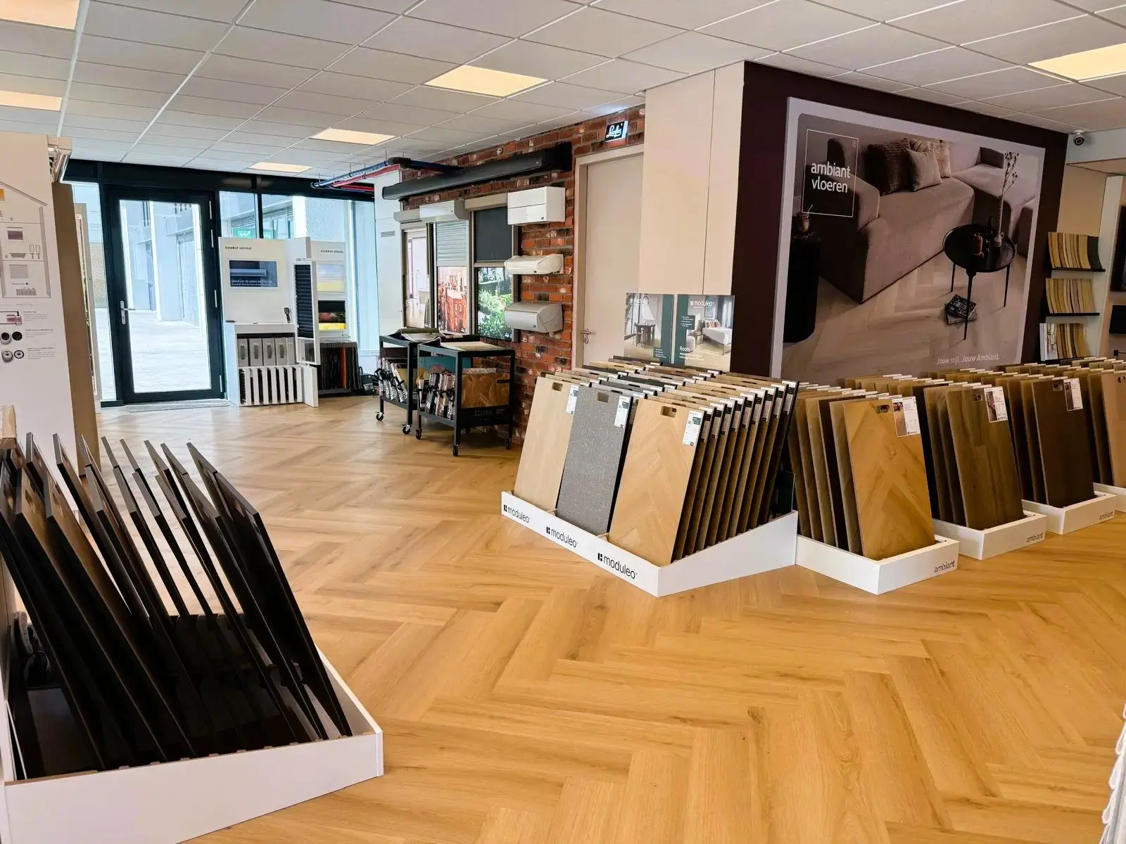 Rekken met grote PVC-stalen in de showroom van Leeuwenkamp, met zonwering aan een stenen wand
